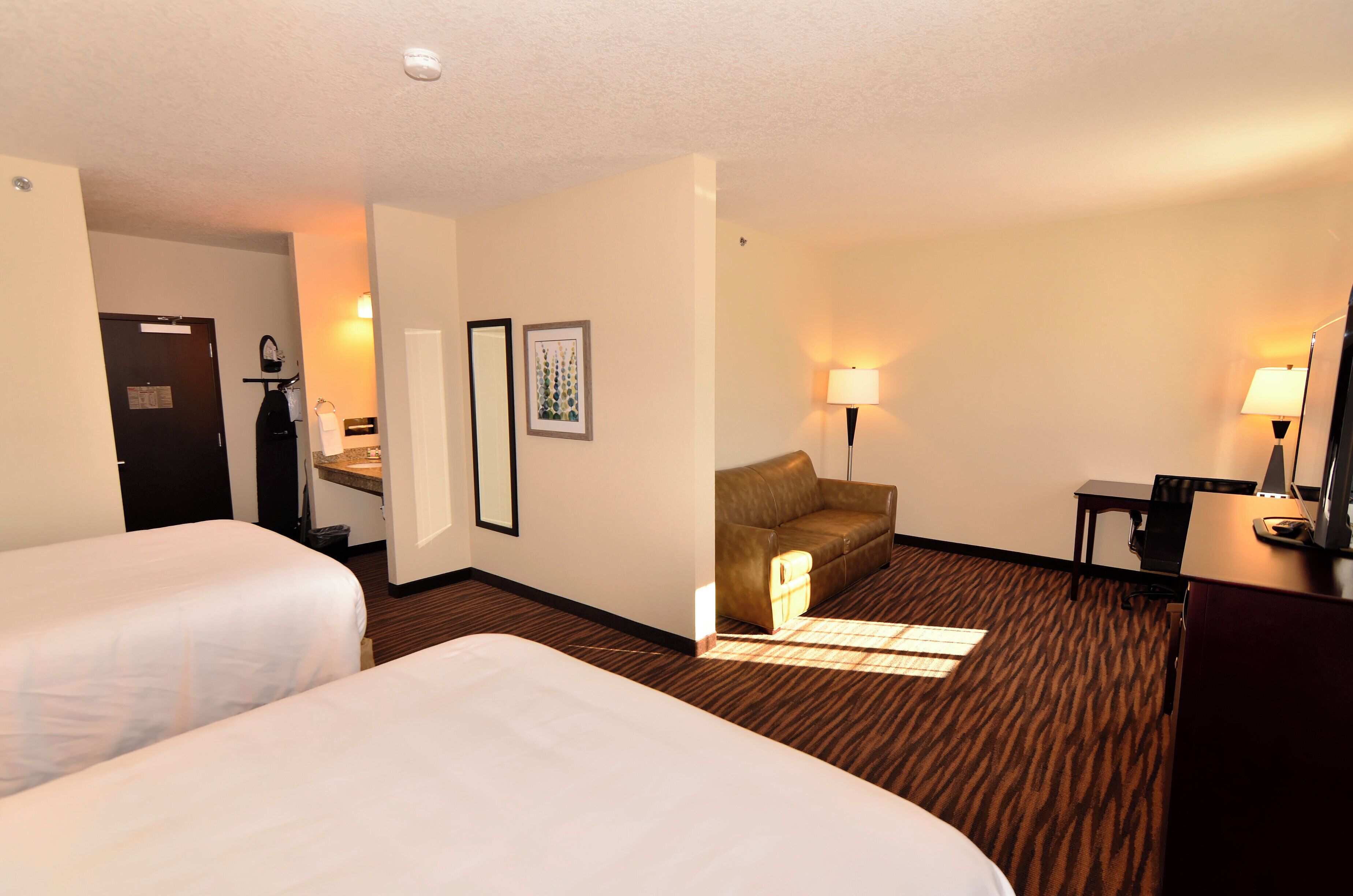 A hotel room with two beds, a sofa, a desk, and a chair.