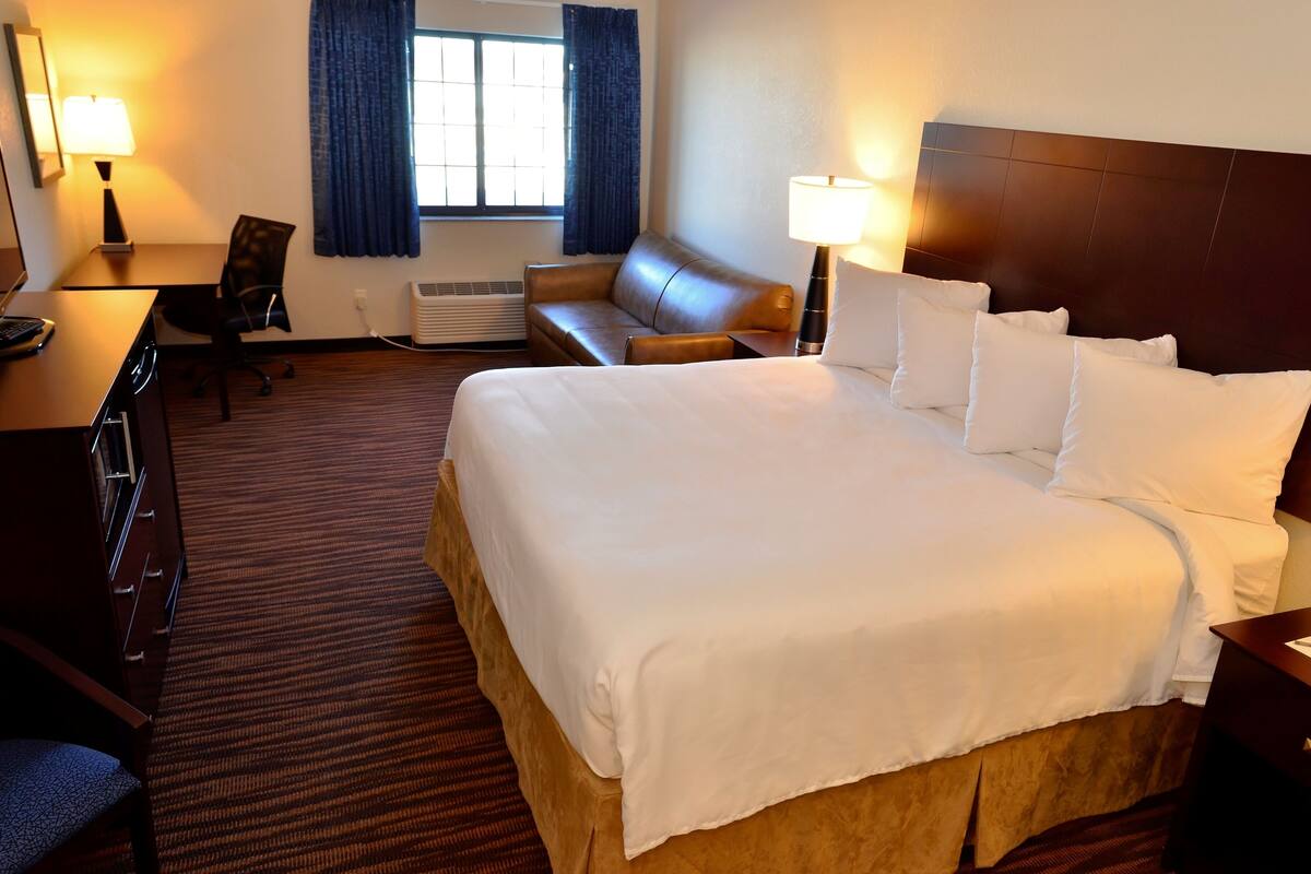 A hotel room with a large bed, a desk, a chair, a sofa, and two lamps.