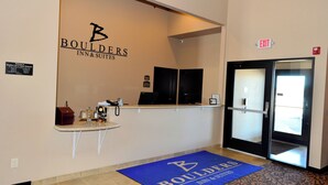 Zona de recepción con un letrero de Boulders Inn & Suites, un mostrador de recepción, una alfombra azul con el logotipo del hotel y una puerta de salida.