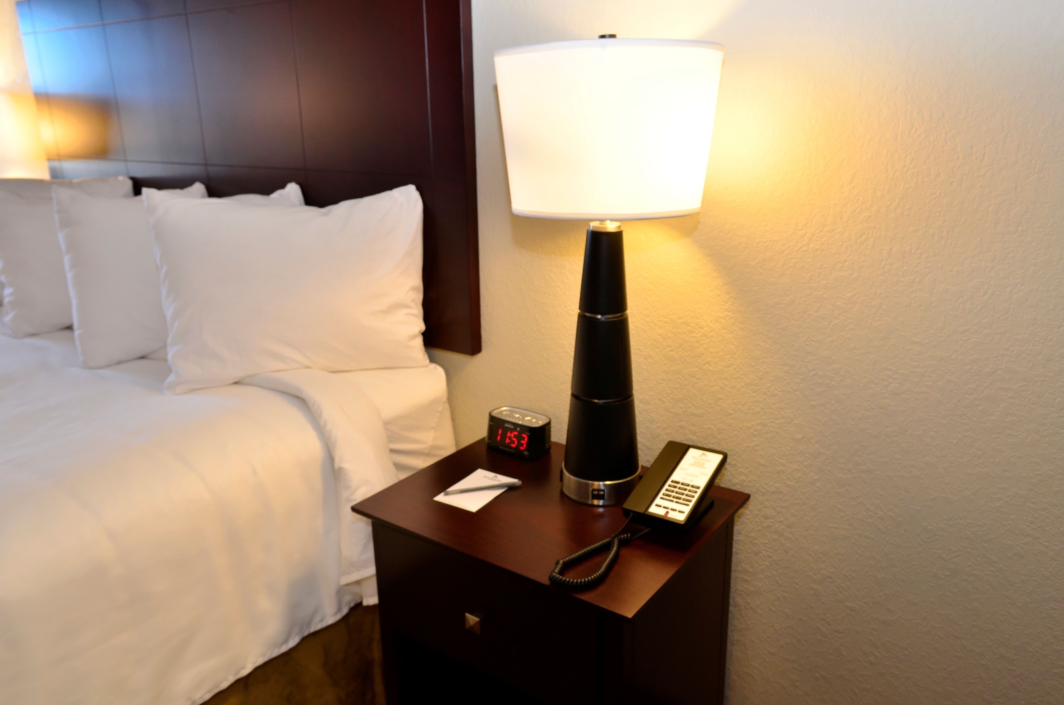 Een hotelkamer met een bed, nachtkastje met lamp, klok en telefoon.