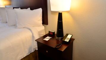 Een hotelkamer met een bed, nachtkastje met lamp, klok en telefoon.