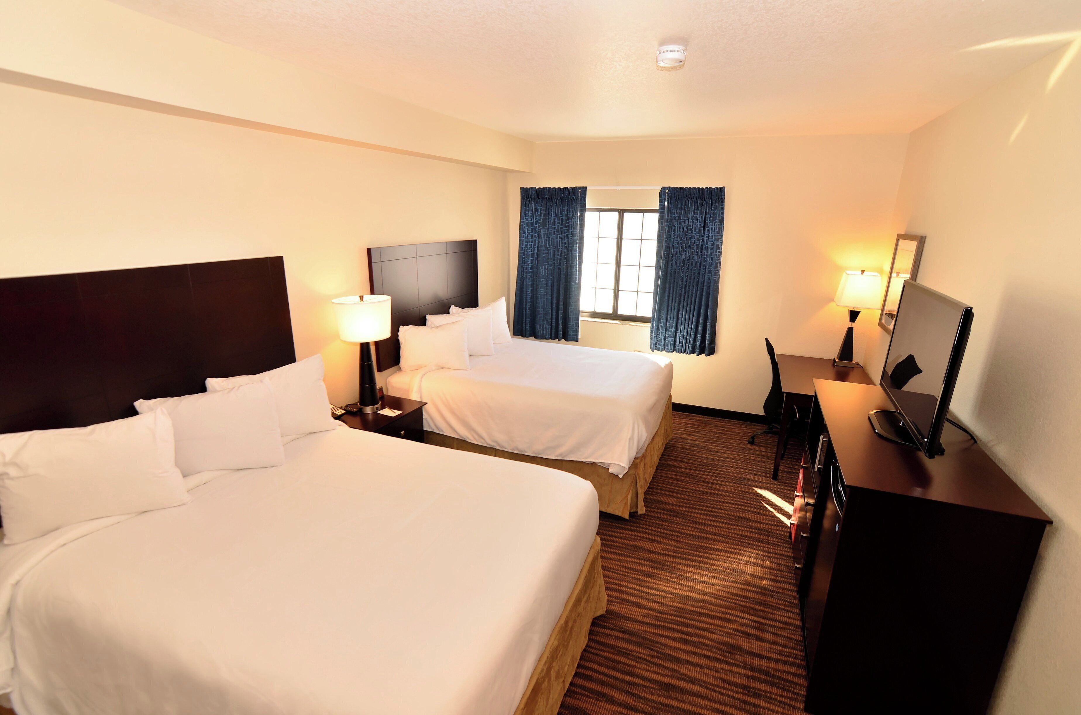 A hotel room with two beds, a desk with a computer, a TV, and a window with curtains.