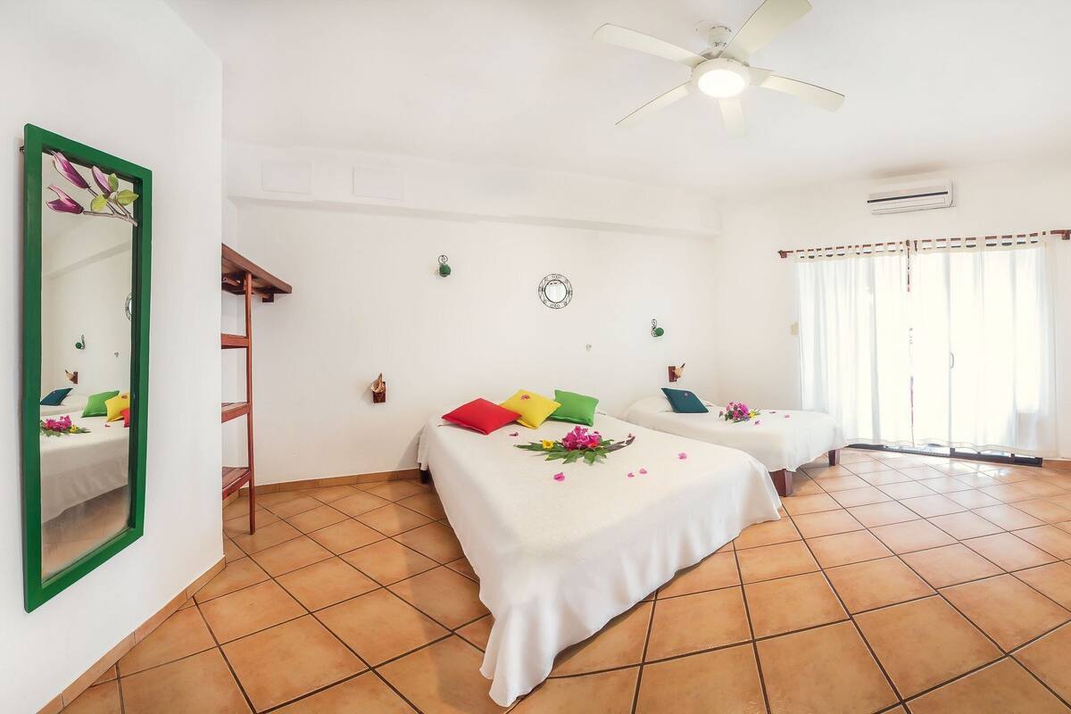 A room with two beds, a ceiling fan, an air conditioning unit, and a window with curtains.