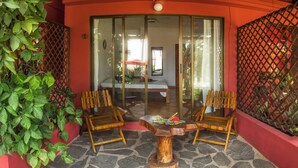A room with a glass door leading to a balcony, two wooden chairs, a small wooden table, and a potted plant. - Laguna del Cocodrilo (Tamarindo)