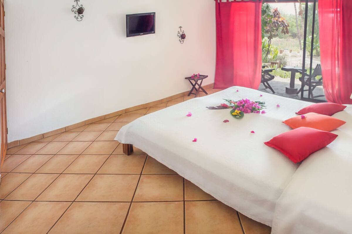 A bedroom with a bed, a TV, a small table, and a window with red curtains.