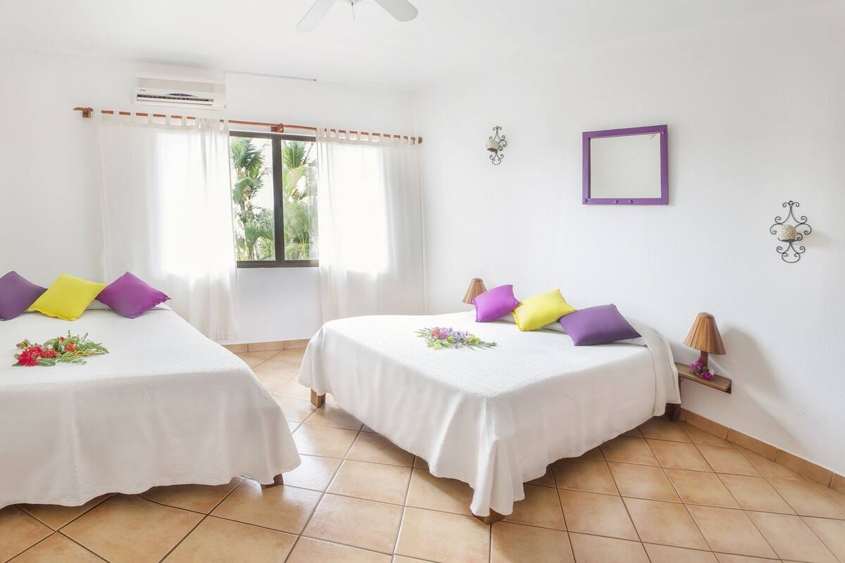 A room with two beds, white bedding, and colorful pillows.