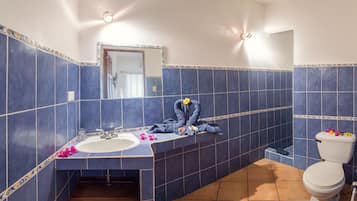 A bathroom with blue tiles, a sink, a mirror, and a toilet.
