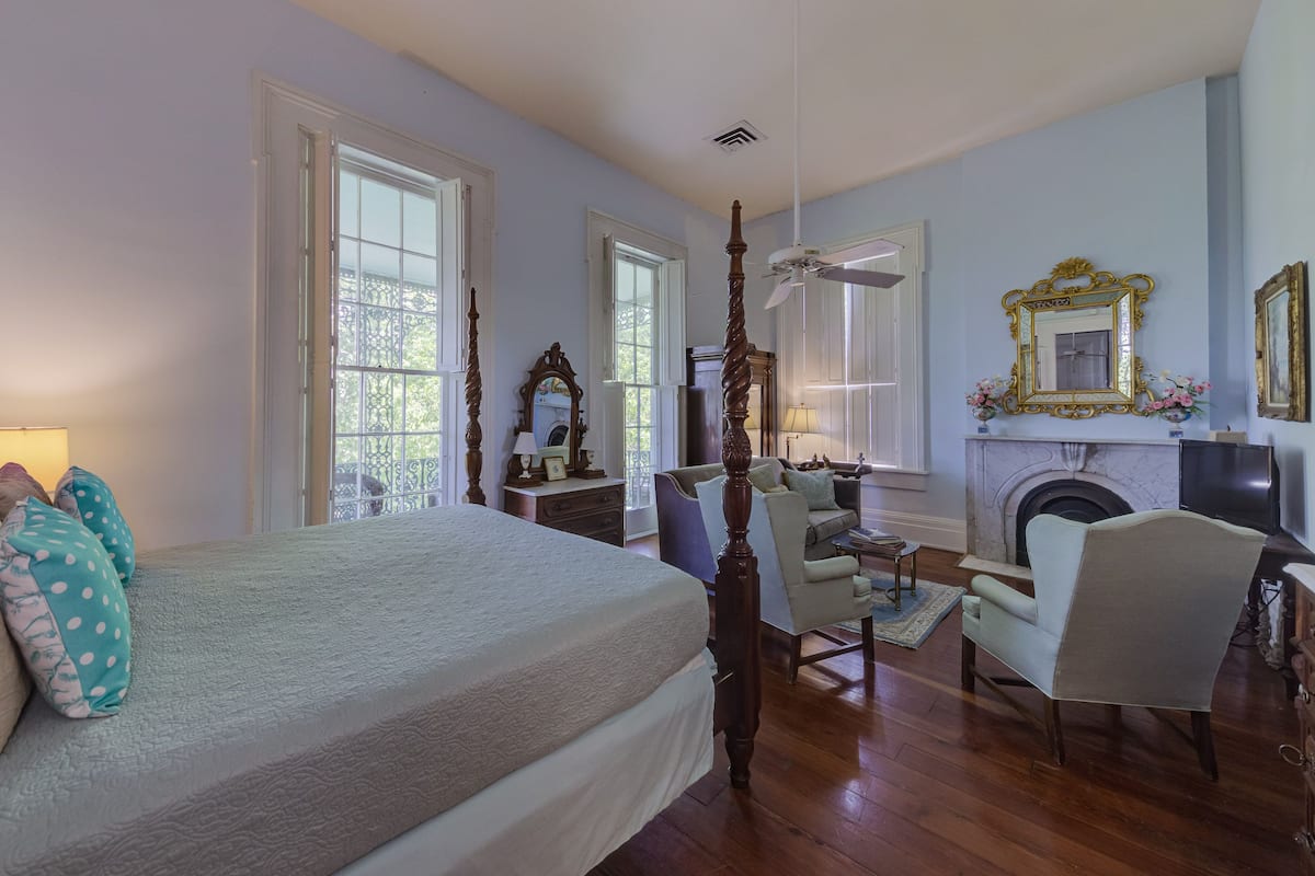 A bedroom with a large bed, a wooden chair, a fireplace, and a mirror on the wall.