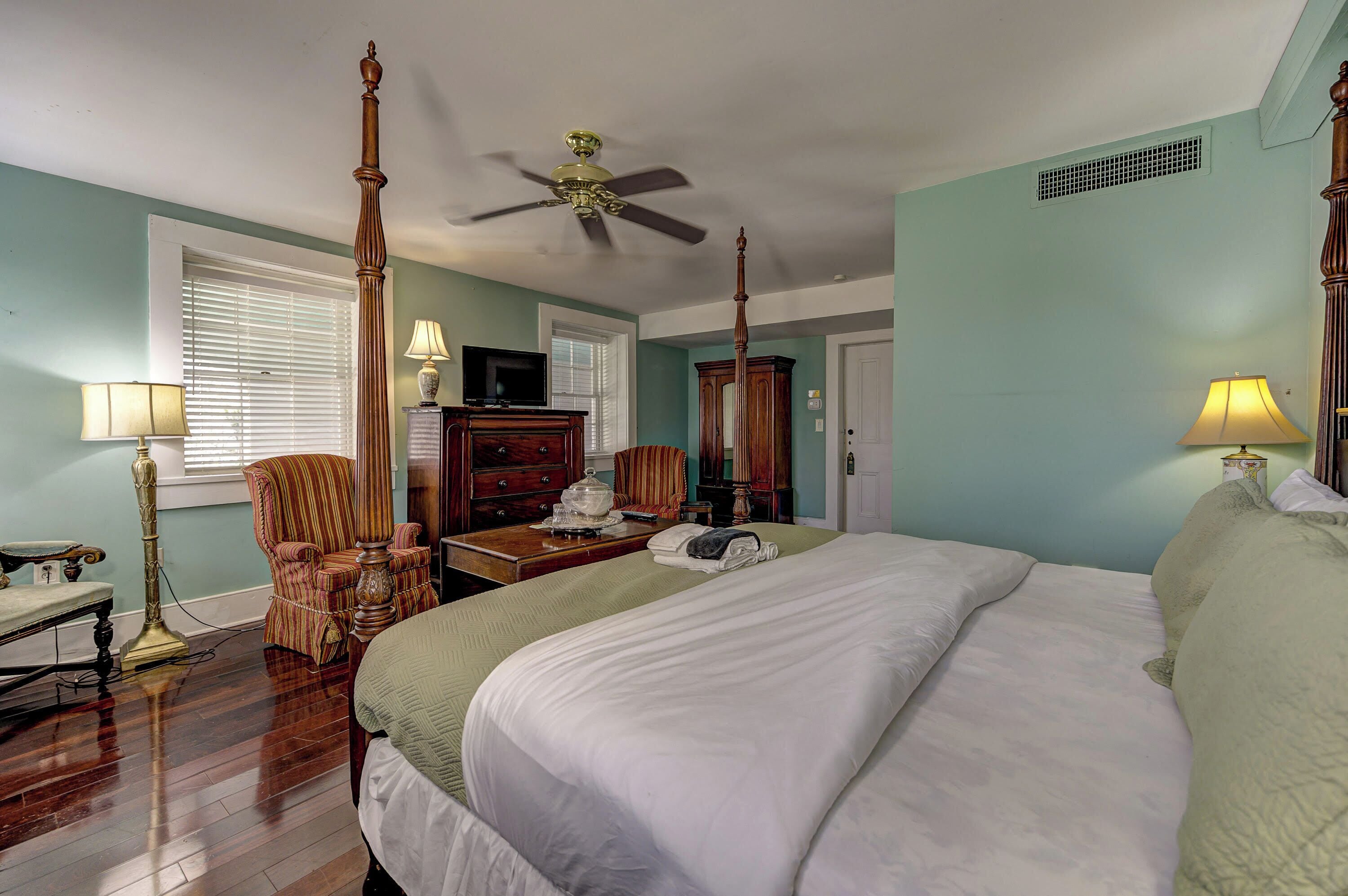 A bedroom with a large bed, a ceiling fan, a television, and a wooden dresser.