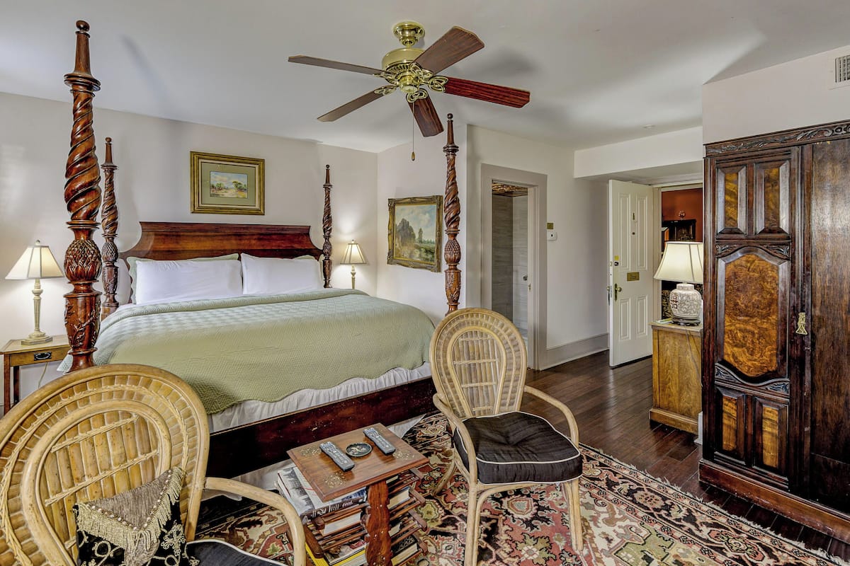 A traditional bedroom with a four-poster bed, a ceiling fan, and a wooden wardrobe.