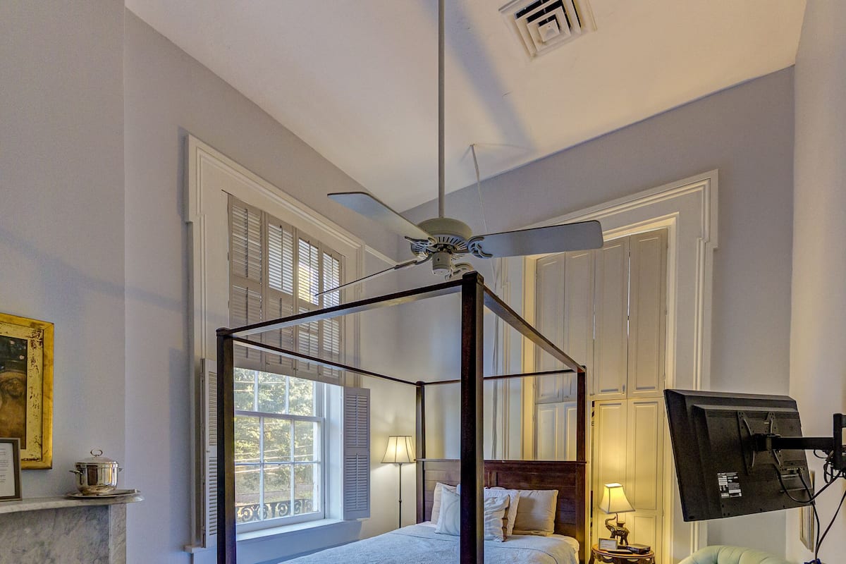 A four-poster bed with a nightstand, a television mounted on the wall, and a green armchair.