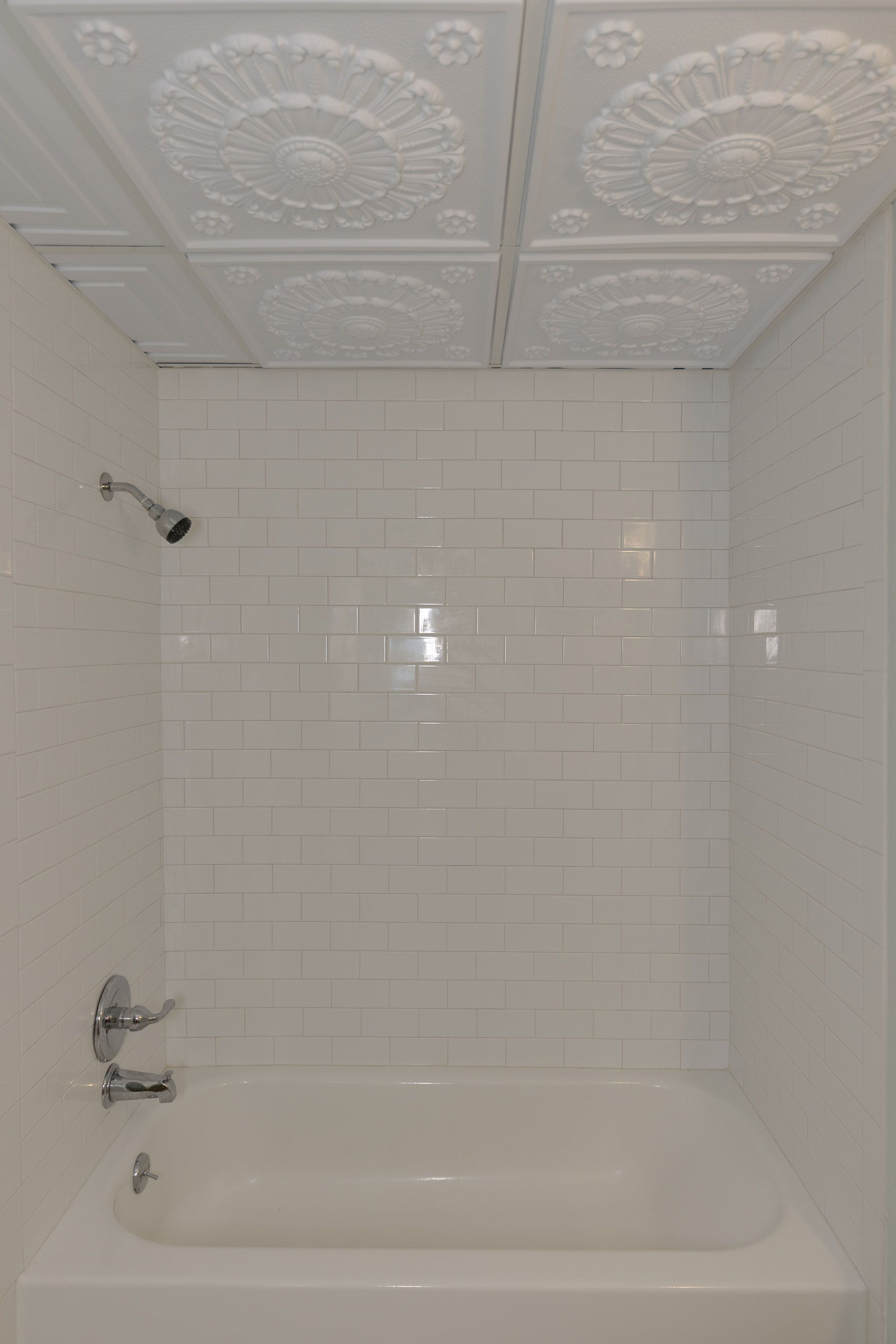 A white-tiled bathroom with a freestanding bathtub, a showerhead, and a wall-mounted faucet.