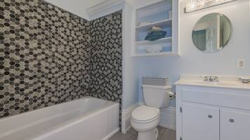 Un baño con bañera, inodoro y tocador con espejo.