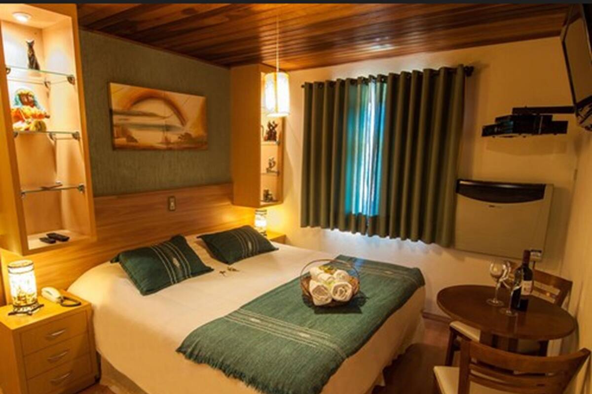 Une chambre d’hôtel avec un lit, une petite table et une chaise, une lampe, une étagère ornée d’une statuette de chat et un tableau accroché au mur.
