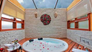 A hot tub with rose petals, a brick wall, and a wooden deck.
