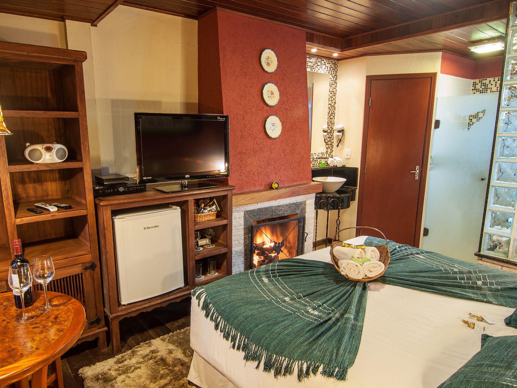 Una habitación acogedora con chimenea, televisión, un refrigerador pequeño y una mesa de comedor con copas de vino.