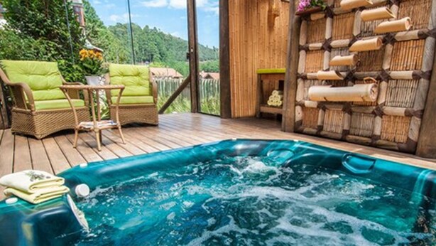Un jacuzzi en una terraza de madera con muebles de mimbre y una pared de bambú.