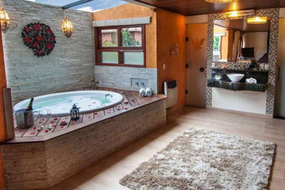 Une salle de bain avec un mur en pierre, un plancher en bois, une grande baignoire, une fenêtre et un miroir.