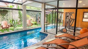 Una piscina interior con paredes de vidrio transparente, rodeada de sillones de descanso y equipo de ejercicio.