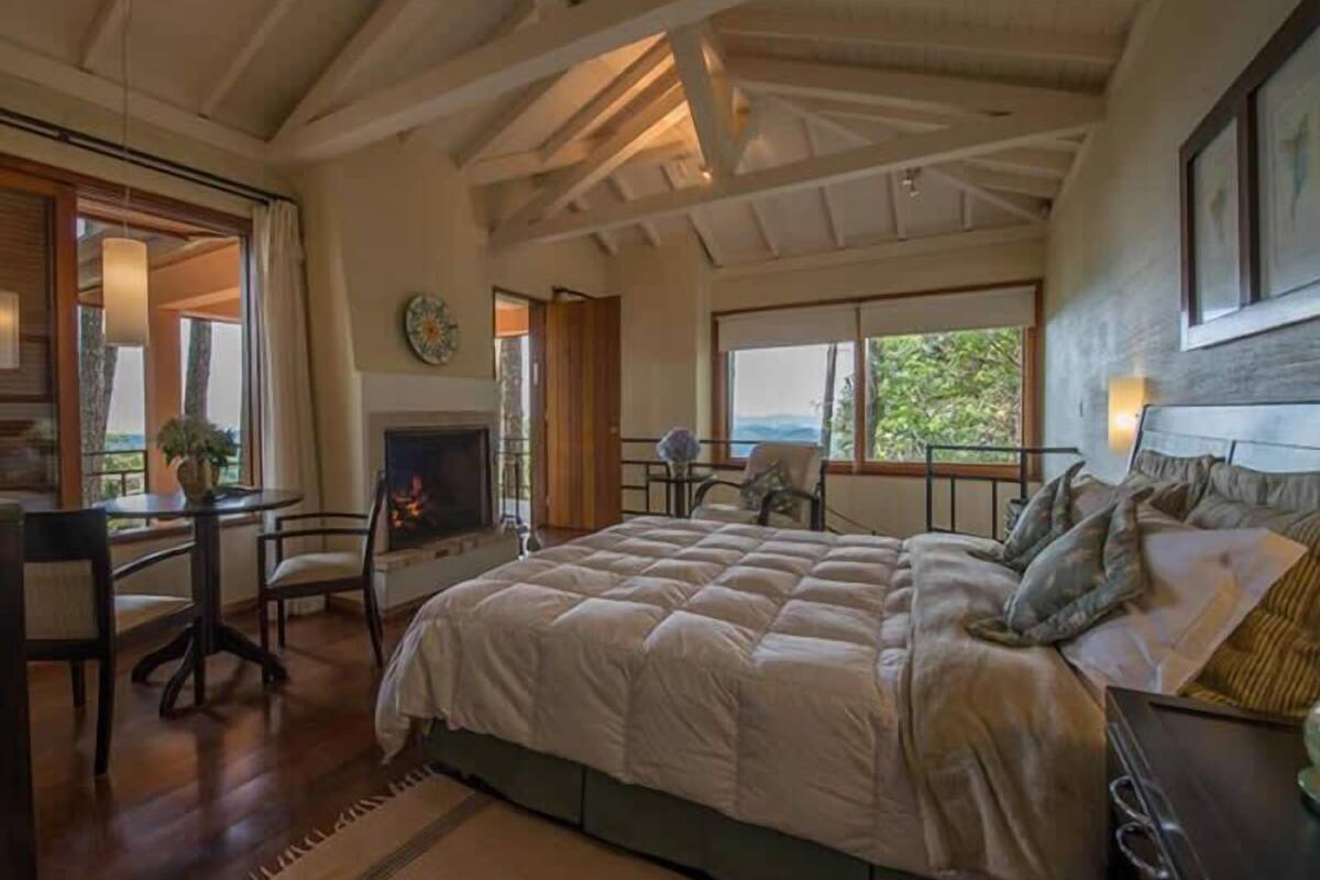 Une chambre dotée d’un grand lit, d’un bureau avec une chaise, d’une cheminée et offrant une vue sur l’extérieur.