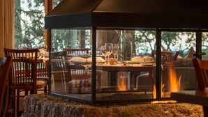 Un rincón comedor acogedor con cerramiento de vidrio, sillas de madera, una mesa dispuesta con platos y vasos, y una chimenea a la vista.