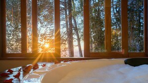 Un jacuzzi con pétalos de rosa en el suelo, un banco de madera y vistas a árboles a través de amplias ventanas.
