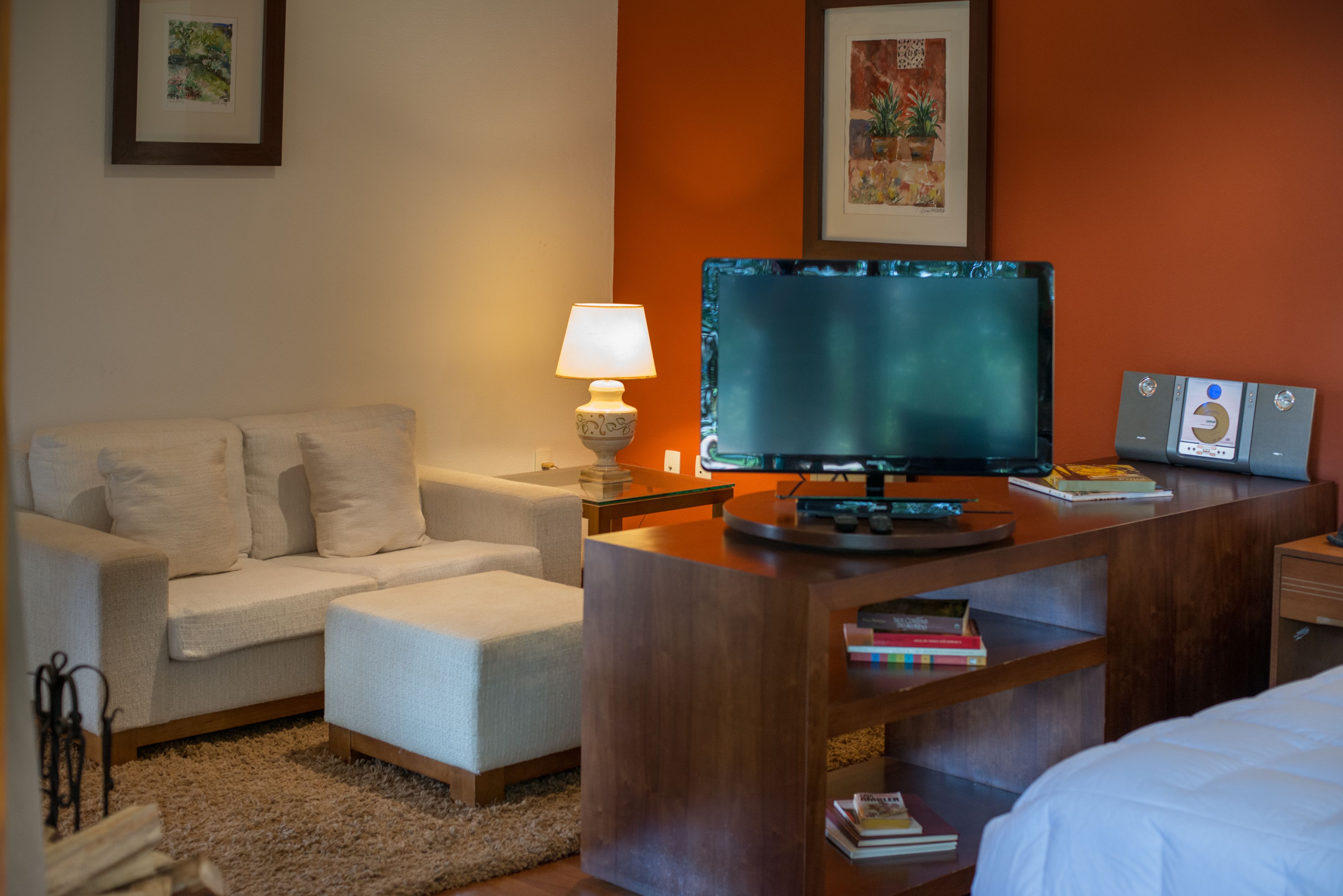 Habitación de hotel con sofá, televisión sobre un soporte de madera, lámpara y estantería con libros.