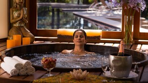 Un espacio de spa con una bañera de hidromasaje, velas, una estatua de Buda y flores.