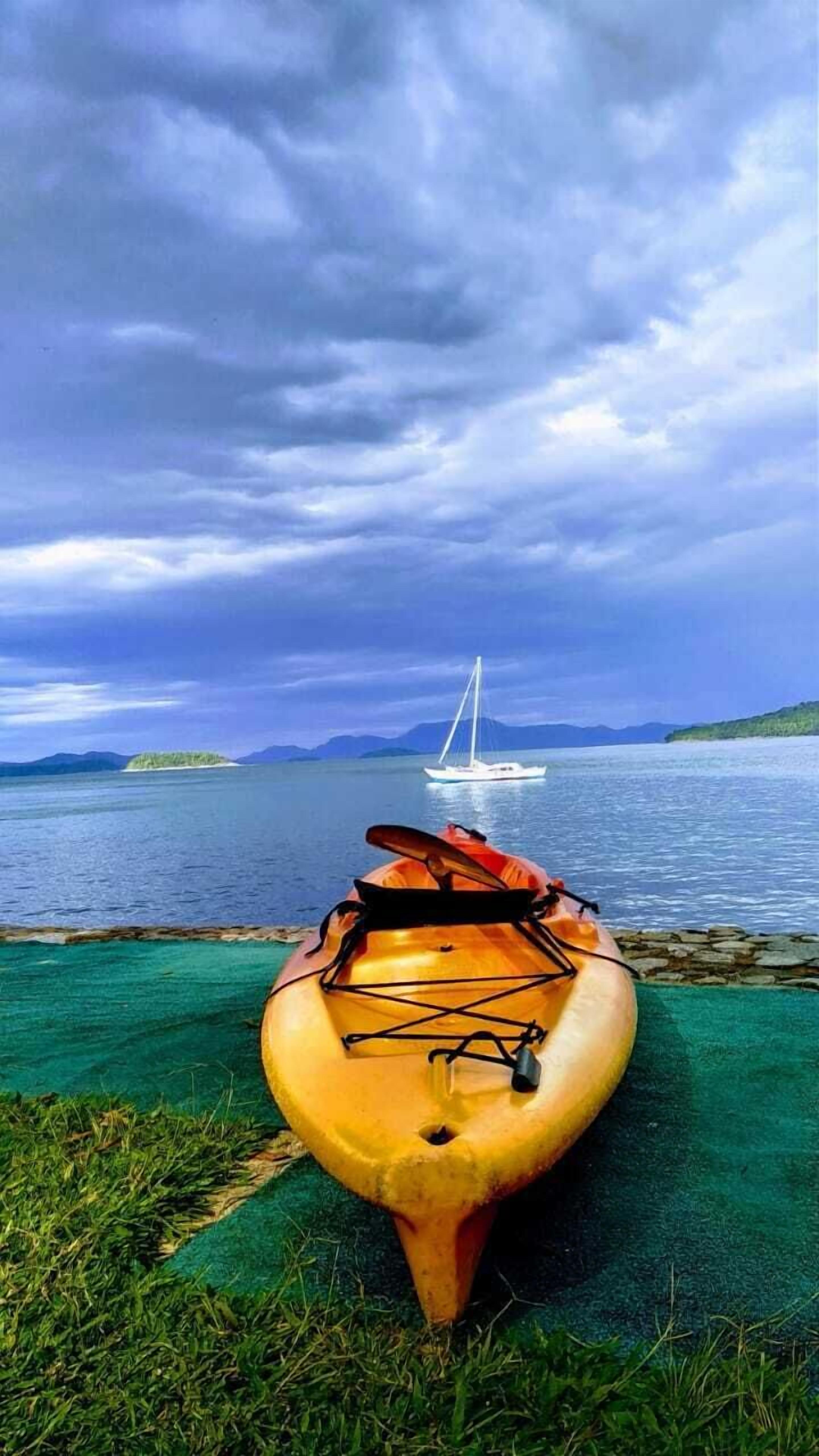 A kayak on a grassy shore with a sailboat in the distance.