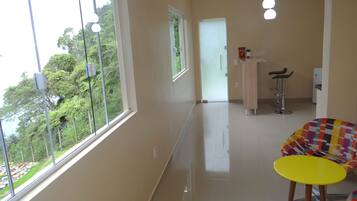 Habitación de hotel con ventanas amplias, una mesa amarilla, una silla colorida y una zona de kitchenette.