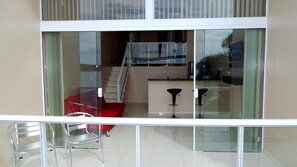 A modern interior with a glass partition, a staircase, a kitchen area, and a red chair. - Ocean Green Flats (Angra dos Reis)