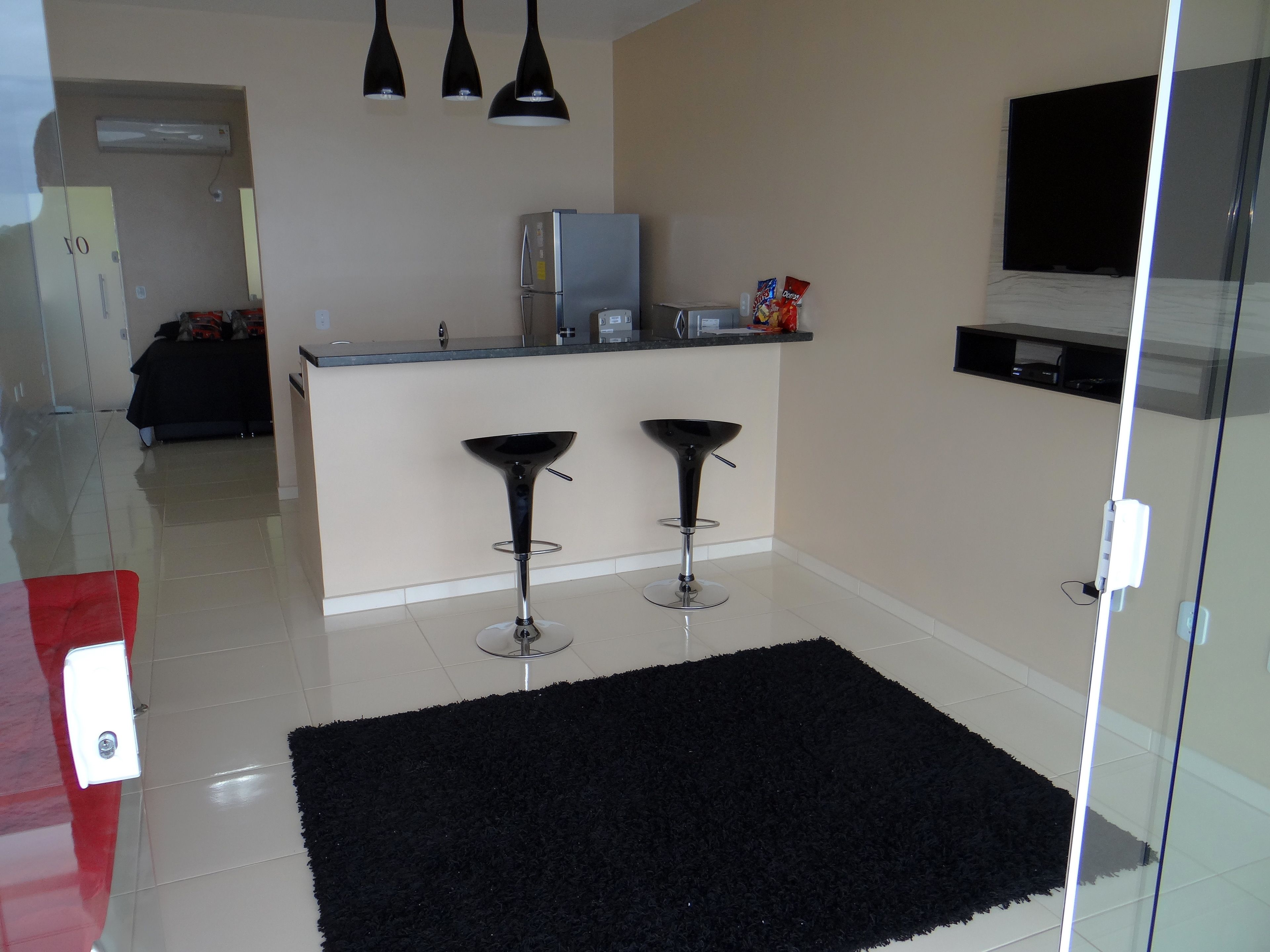 A modern kitchen with a black countertop, two bar stools, a refrigerator, and a TV mounted on the wall.