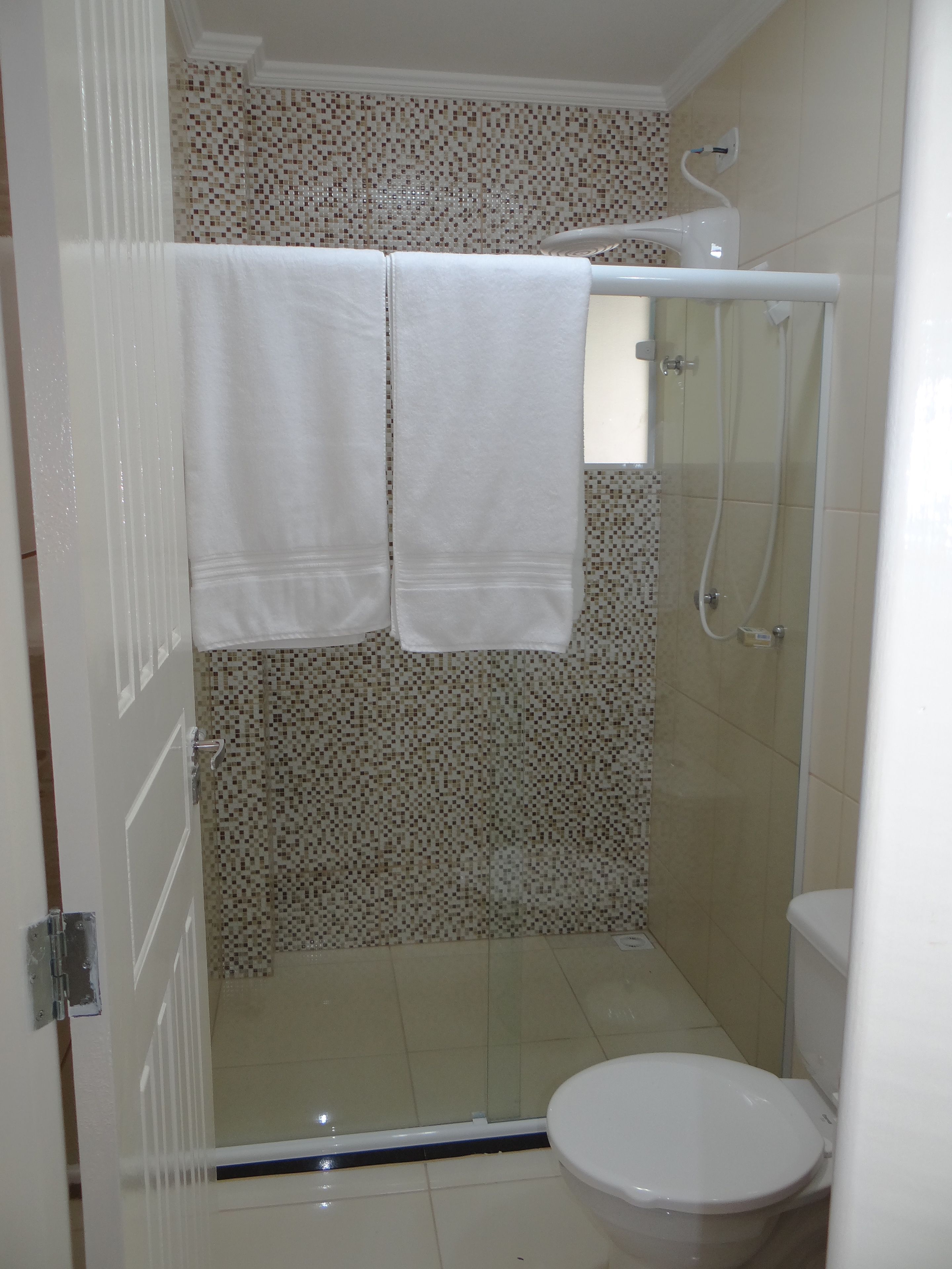 Un baño con ducha, inodoro y pared de azulejos.
