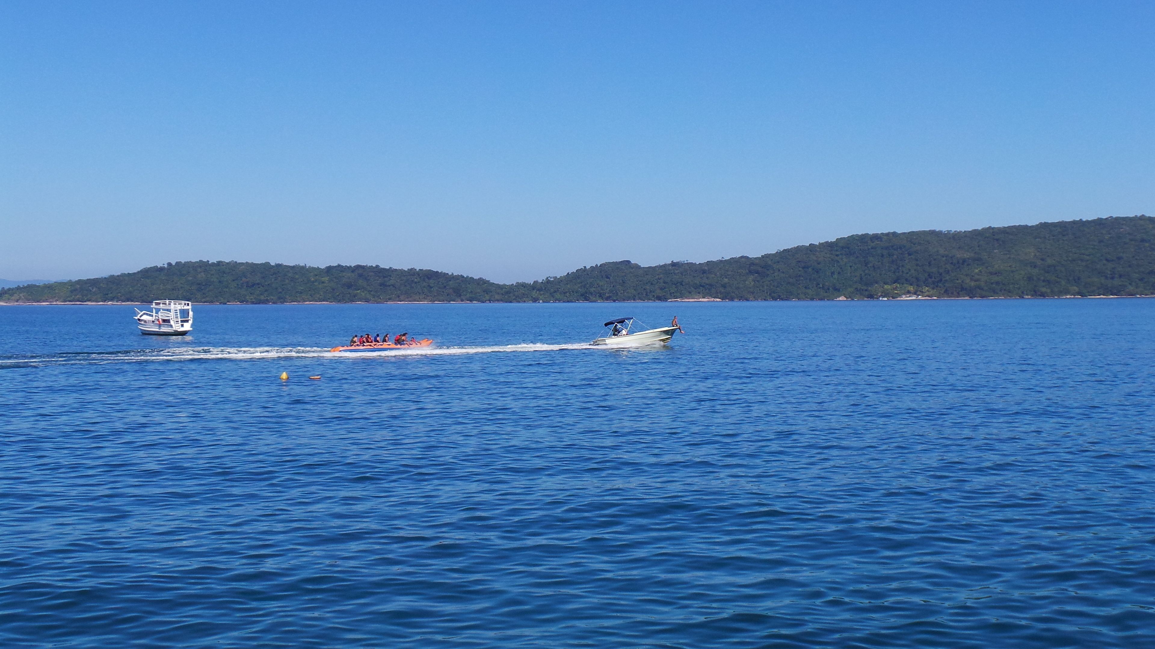 A boat with passengers on a calm sea, a smaller boat in the background, and a forested coastline.