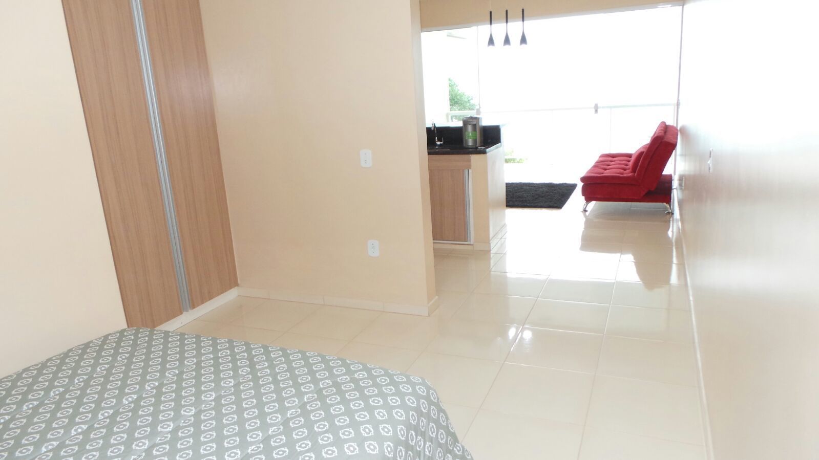 A bedroom with a bed, a kitchenette, and a red chair.