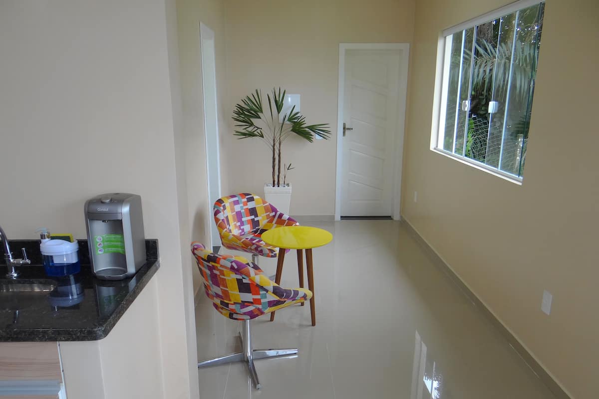 A clean, modern kitchen with a coffee machine, a colorful chair, a small table, and a potted plant.