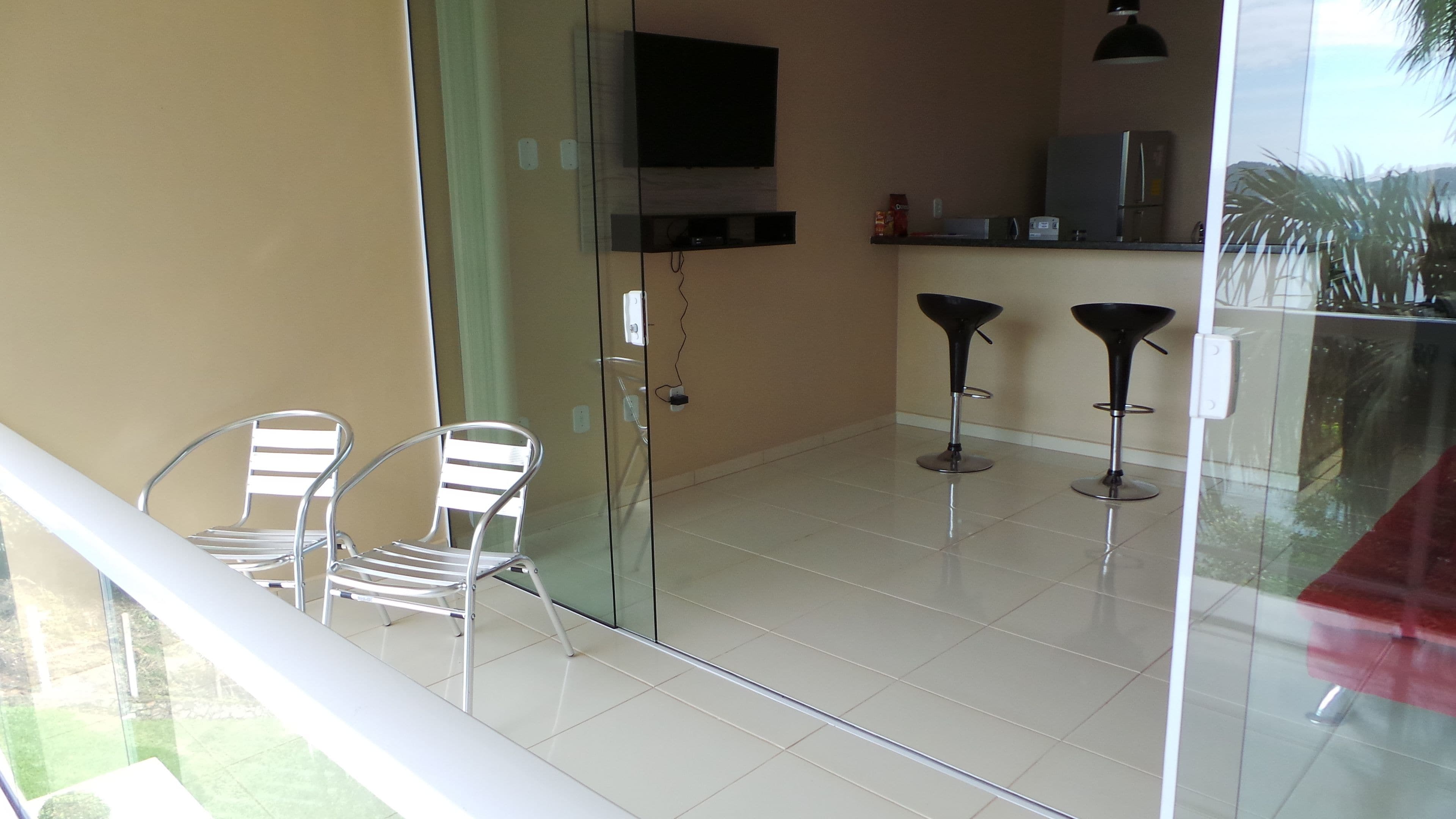 A modern kitchen with a flat-screen TV, two bar stools, and a glass door leading to a balcony.
