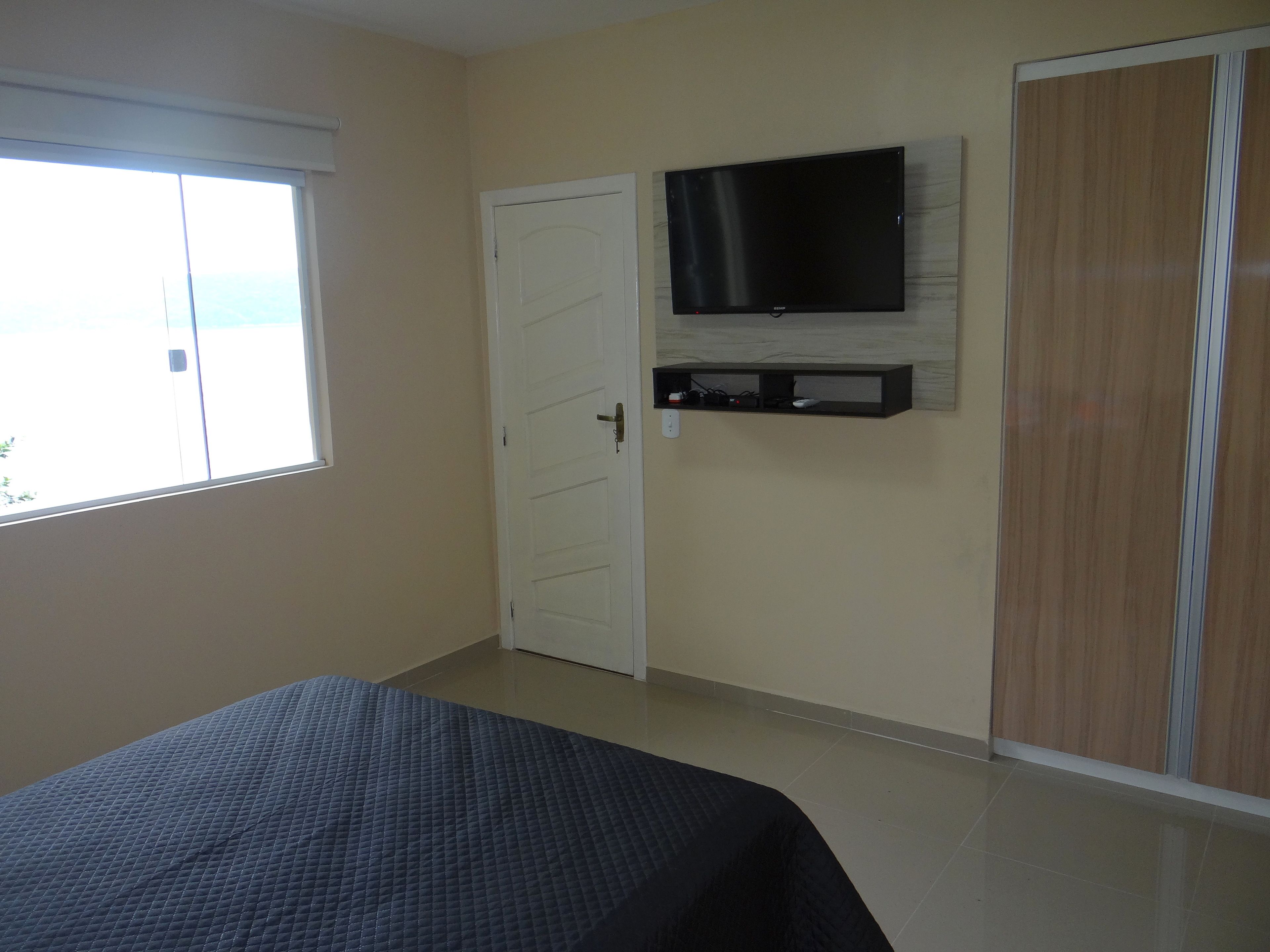 A bedroom with a bed, a TV mounted on the wall, a wardrobe, and a window.