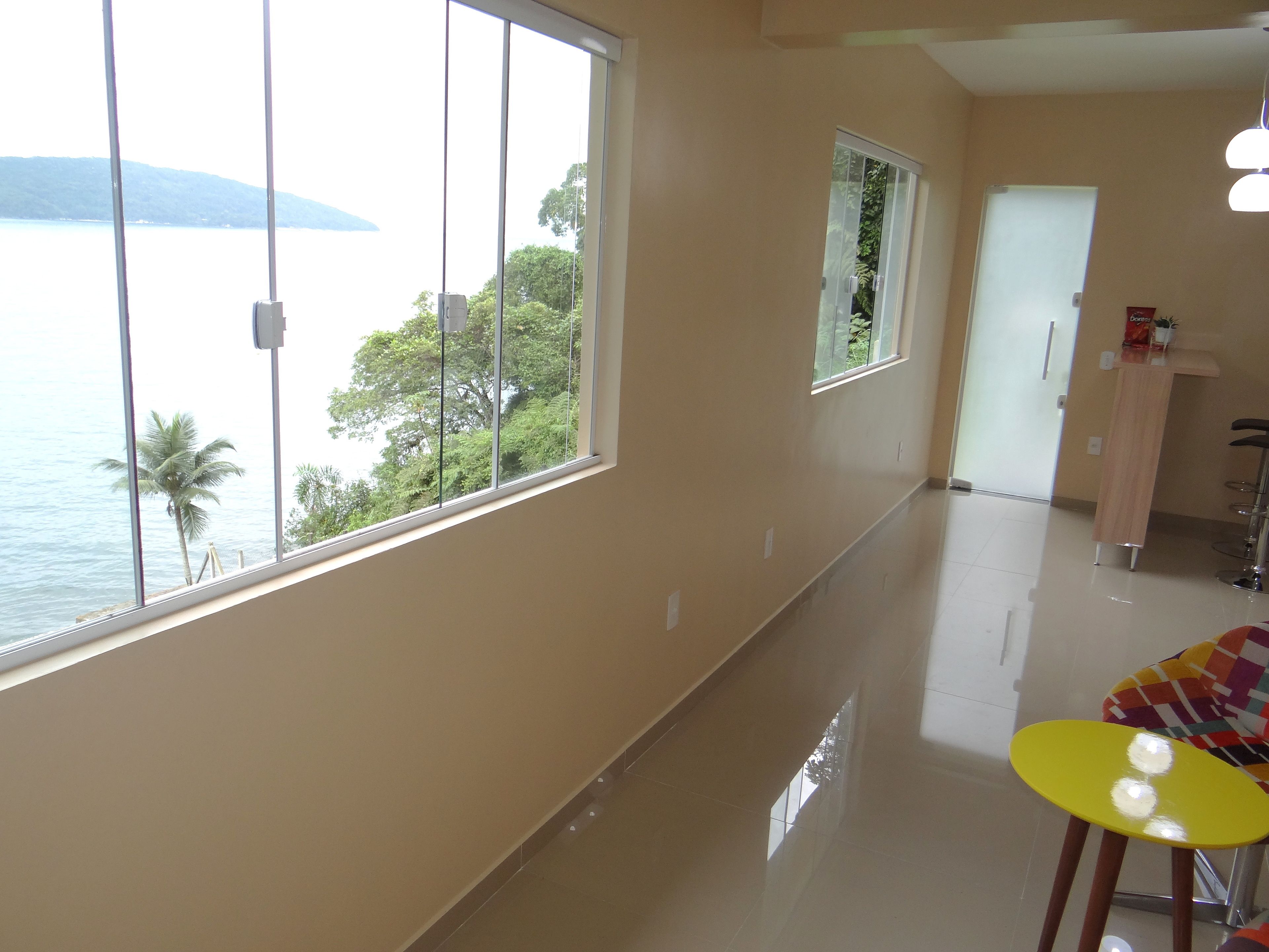 A hotel room with large windows offering a view of the sea and palm trees.