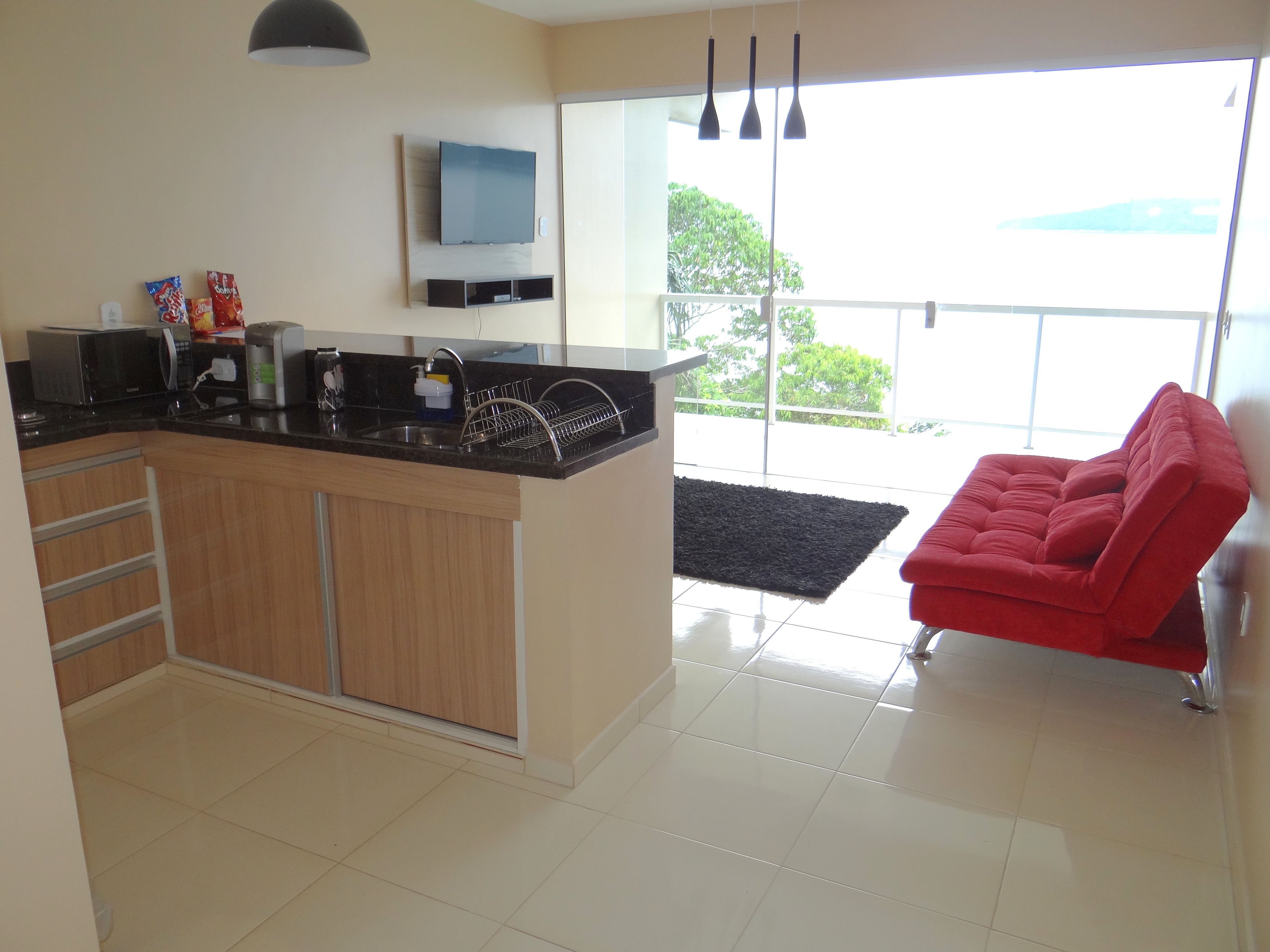 A modern kitchen with a built-in oven, microwave, and coffee maker. There is a red chair and a black rug in the living area.