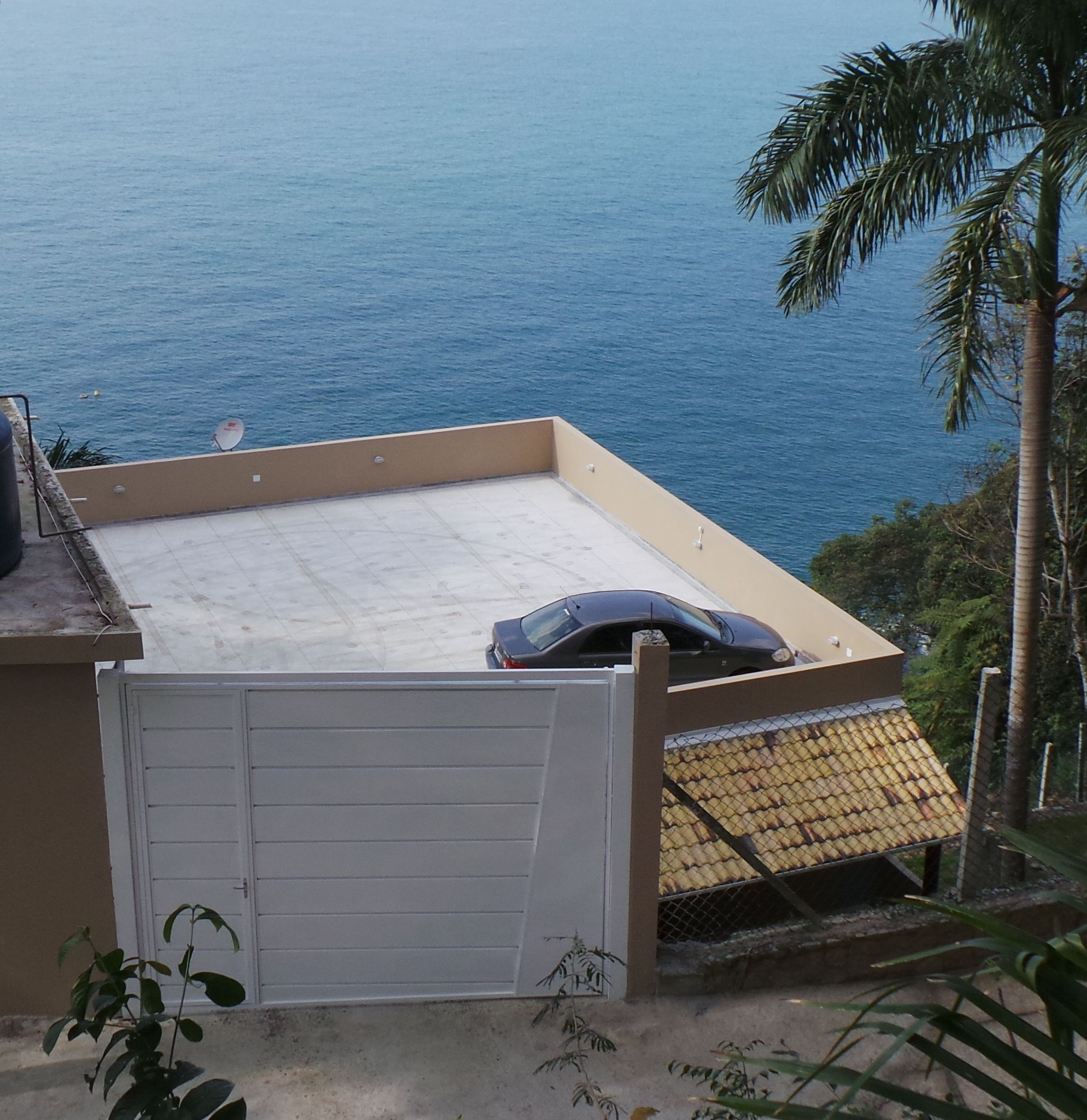A rooftop terrace with a car parked on it, overlooking the sea.