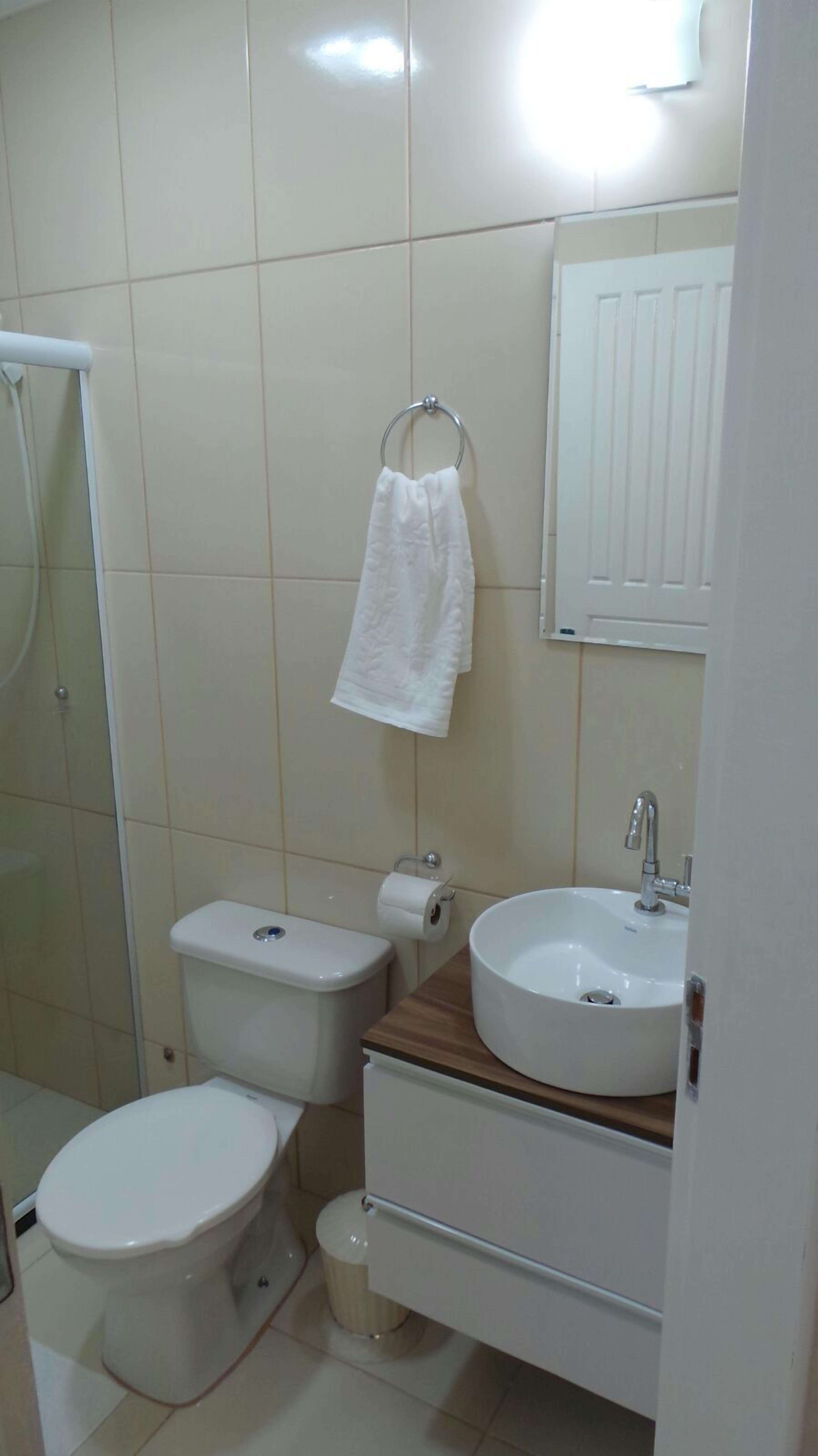 A bathroom with a toilet, bidet, sink, and a towel hanging on a metal ring.