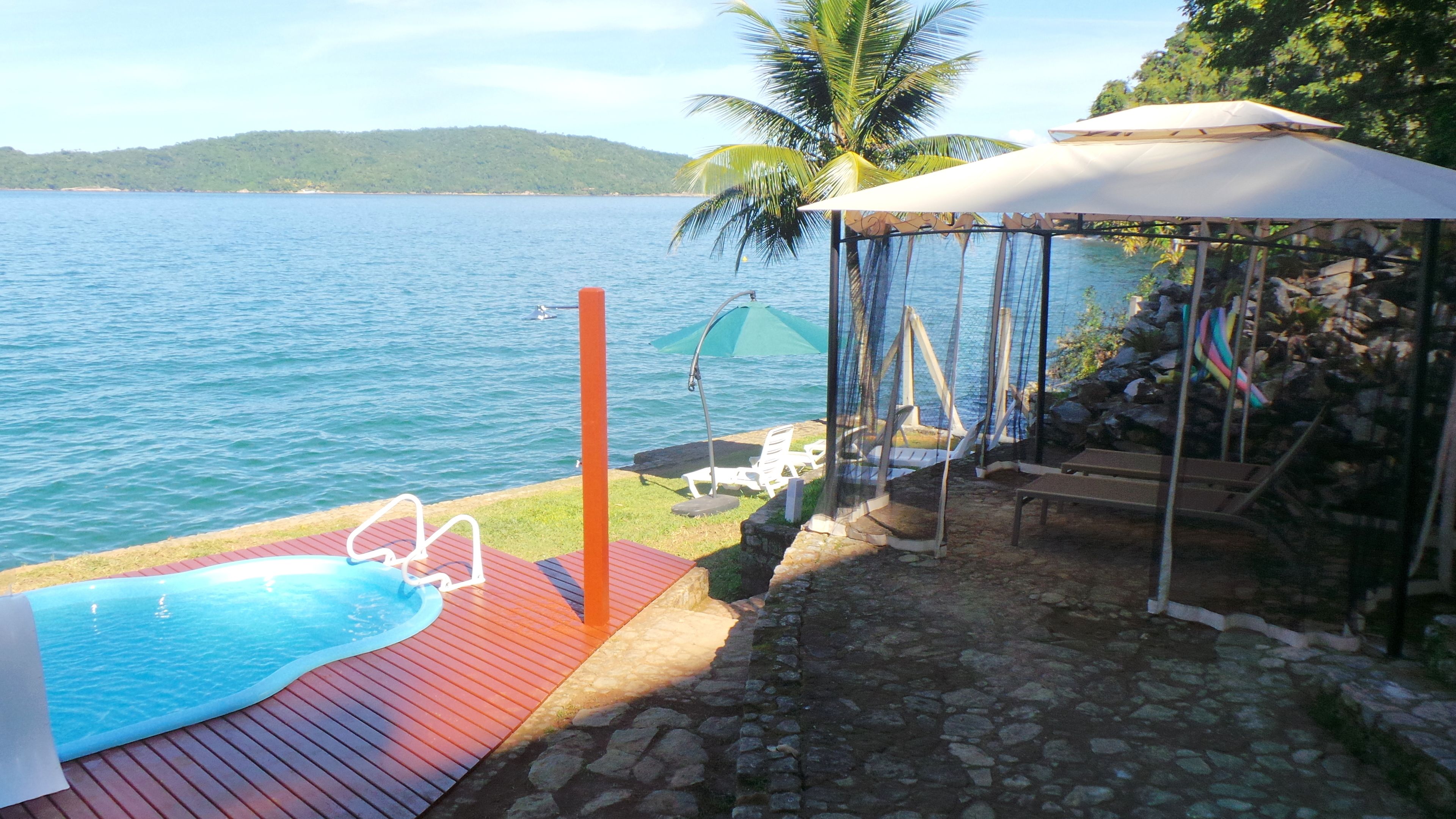 Un espace piscine doté d’une terrasse en bois, d’un coin salon abrité et d’une vue sur la mer.