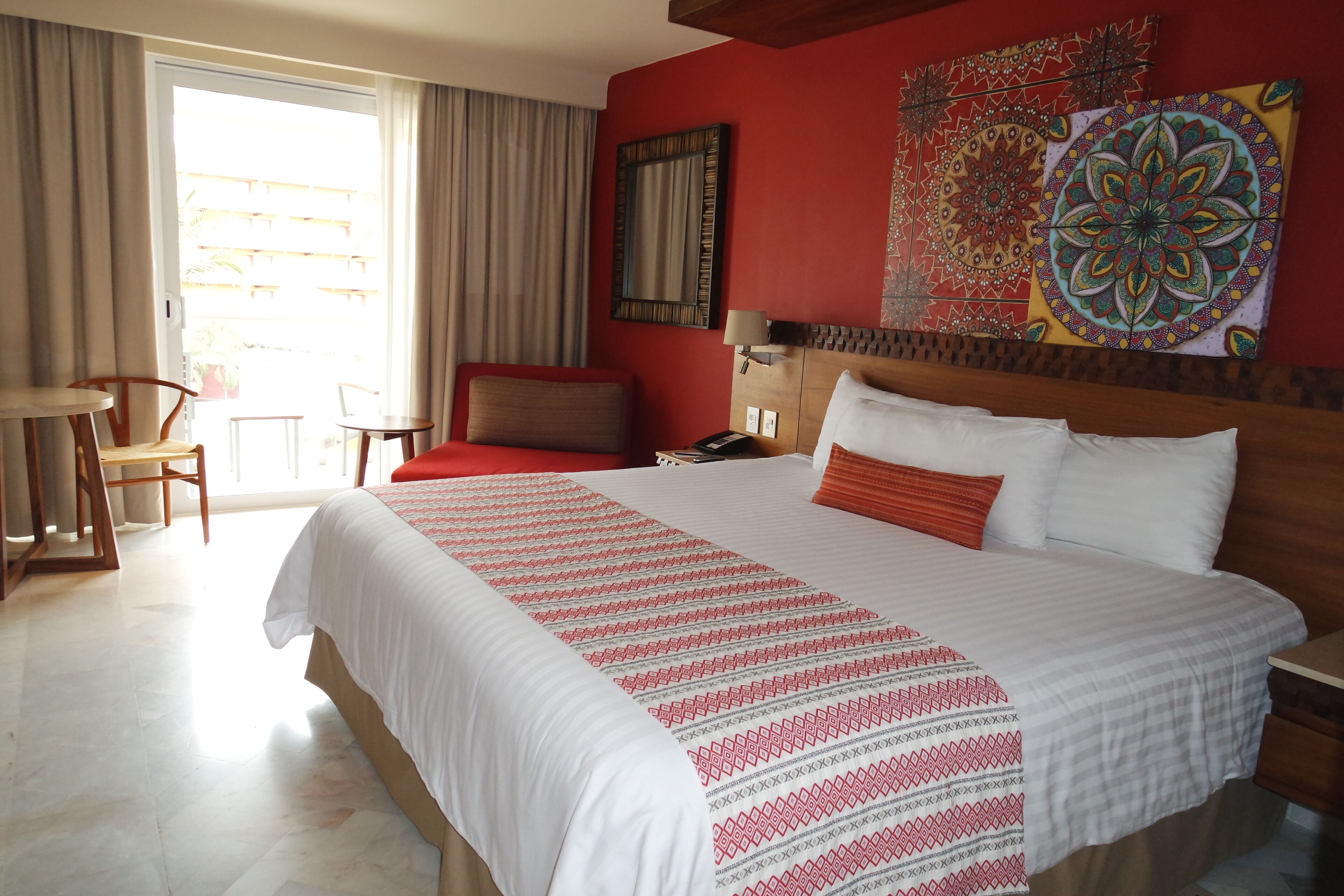 A hotel room with a large bed, a desk, a chair, and a view of the outside.