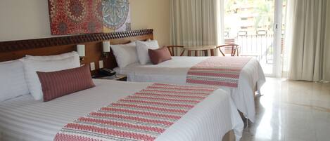 A hotel room with two beds, a wooden headboard, a table with chairs, and a view of the outside balcony.