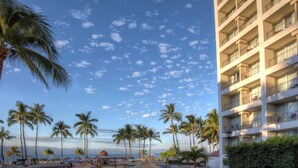 A hotel with multiple balconies, palm trees, and a beach view.
