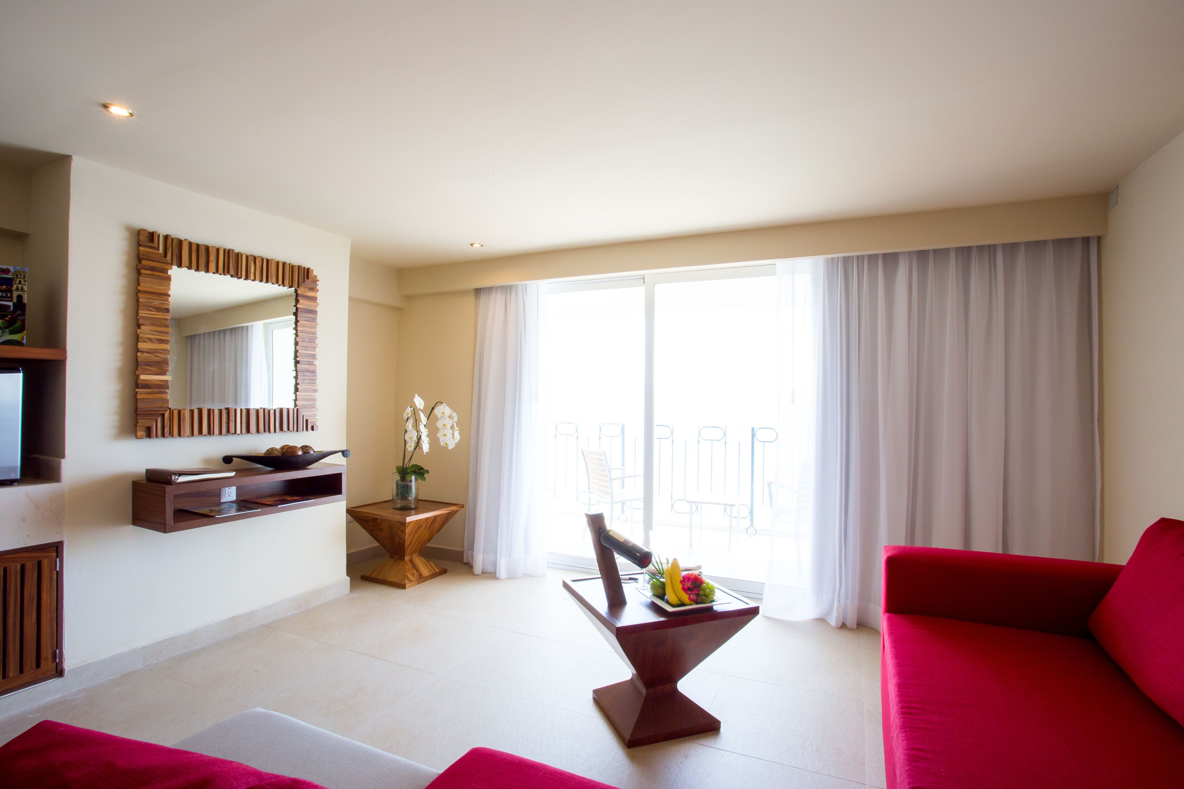 A modern living room with a red sofa, a wooden coffee table with fruit, a TV, and a large window with curtains.