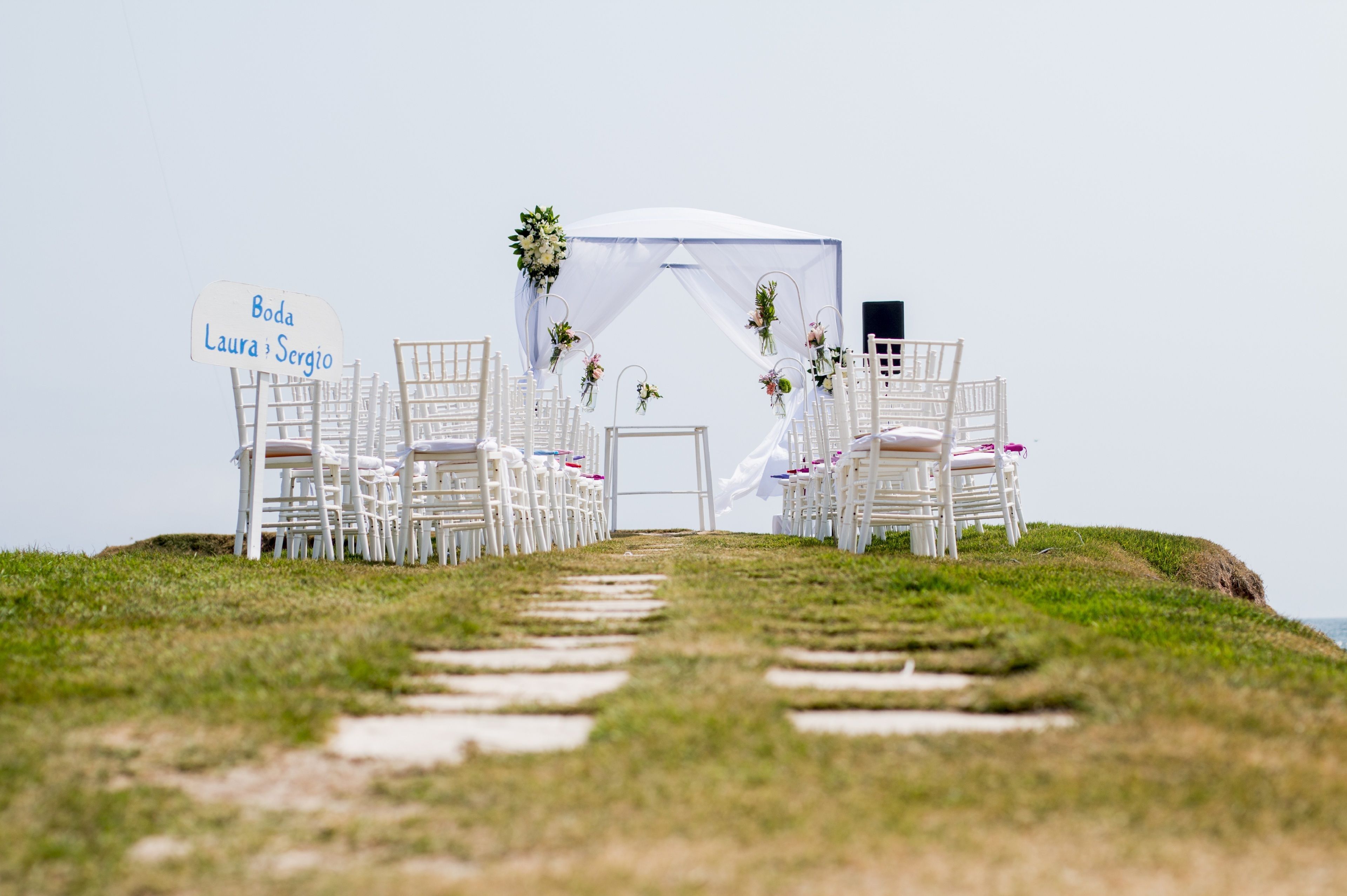 Une cérémonie de mariage a été organisée avec des chaises blanches et un dais, le tout installé sur une colline verdoyante offrant une vue sur la mer.
