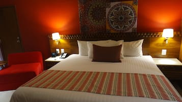 A hotel room with a large bed, two bedside tables, a red chair, and a decorative tapestry on the wall.