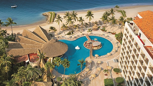 A resort with a large pool, palm trees, and a beach.